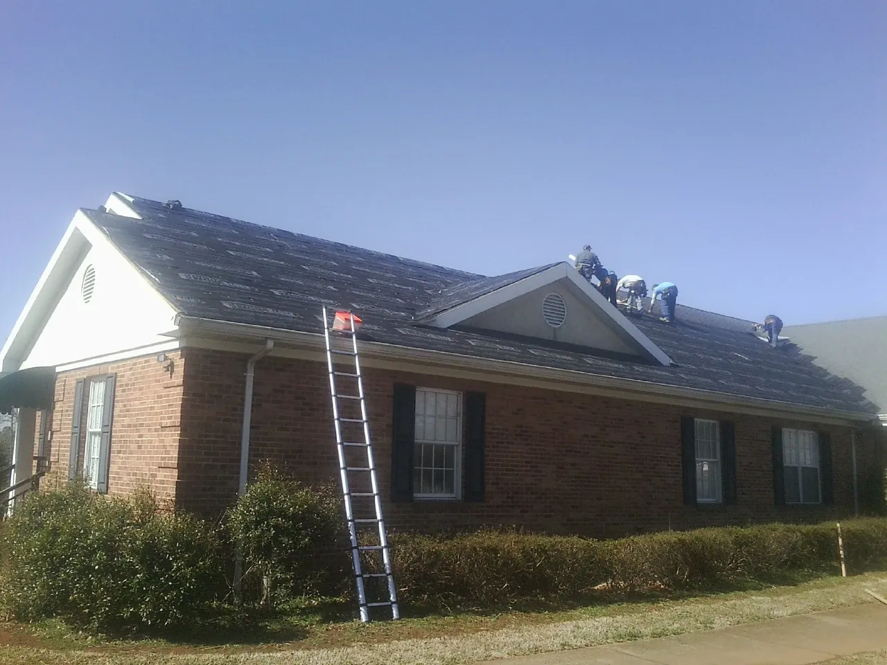 Crew tearing shingles off a brick ranch roof with a ladder set — Metal Roof Repair work by our crew in Lynden