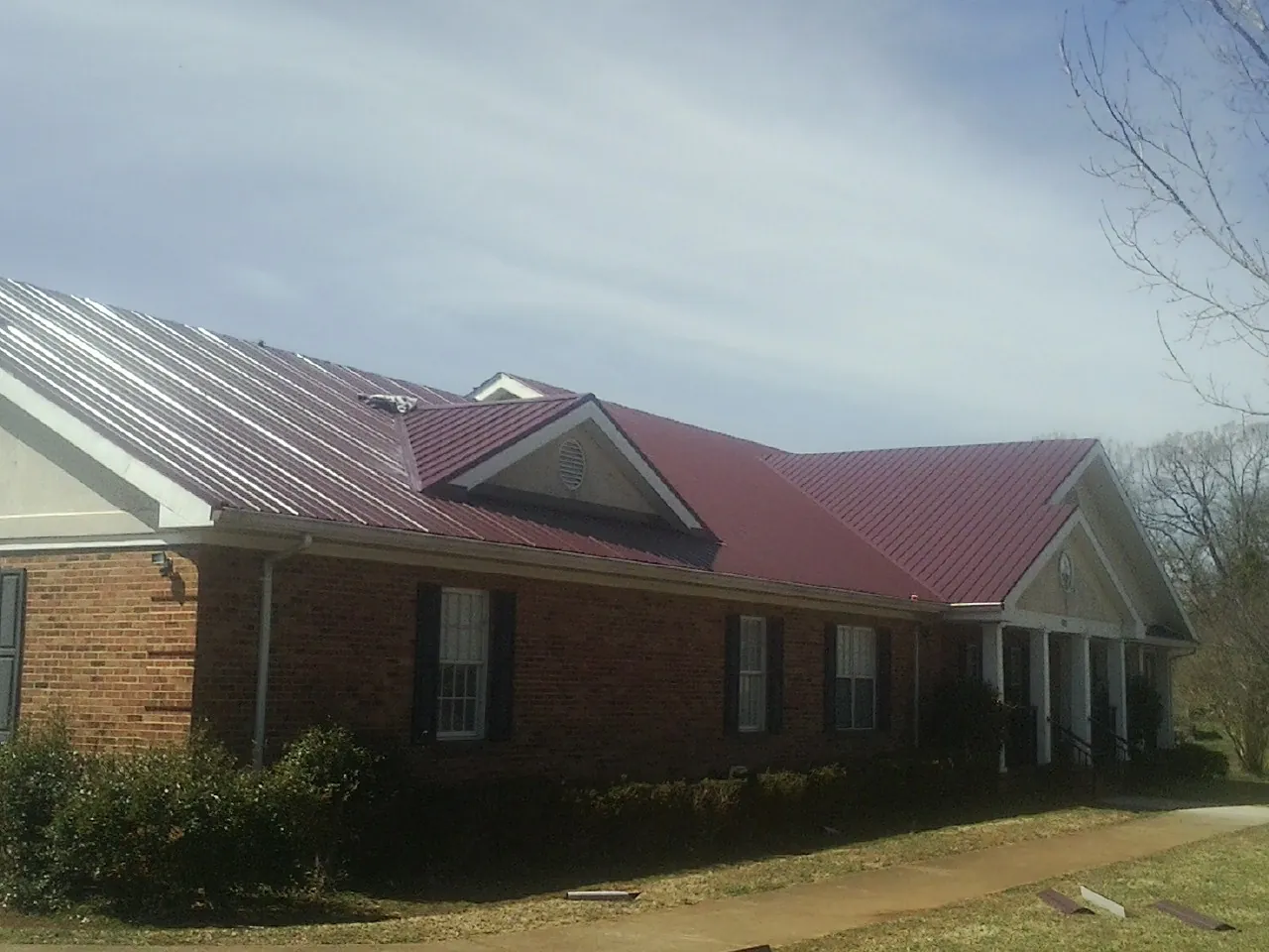 Red metal roof with gabled entries on a long brick building, from a Hail Damage Roof Repair job in Lynden