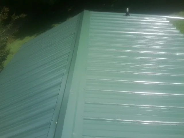 New green metal panels meeting at the ridge of a roof — Flat Roof Repair work by our crew in Lynden