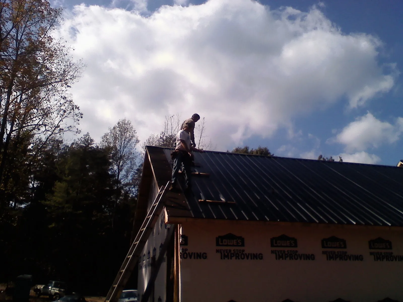 Roofer fastening dark metal panels high against a cloudy sky, from a Roof Inspection job in Lynden