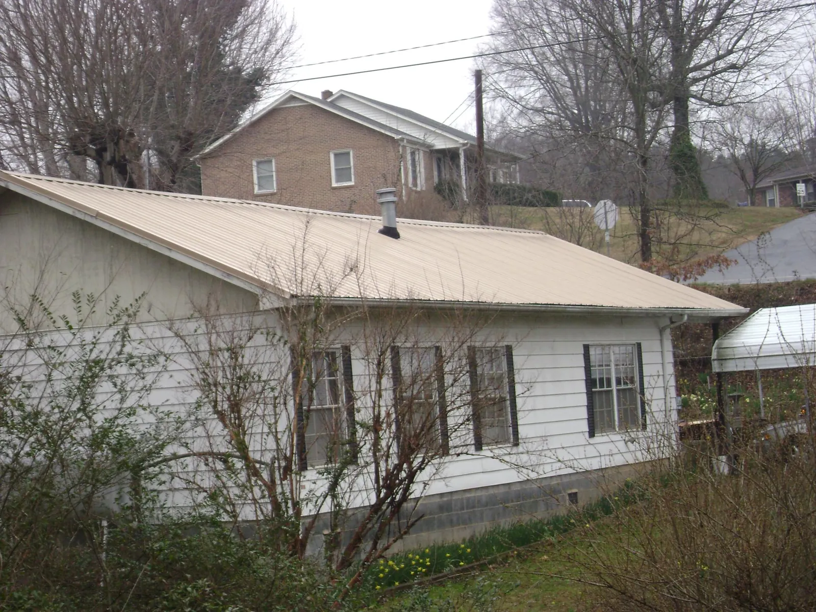 Tan metal roof on a white sided house set into a hillside — Commercial Roofing by Roofing Brothers in Lynden